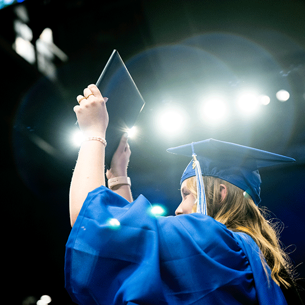 A woman holding her diploma in the air.