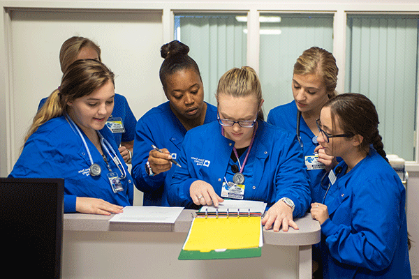 A group of six nursing students all look over a chart