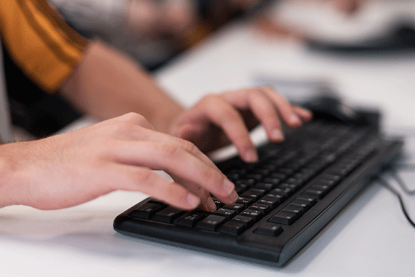 A detailed photo of a black laptop keyboard on a white table with two hands resting on the keyboard.