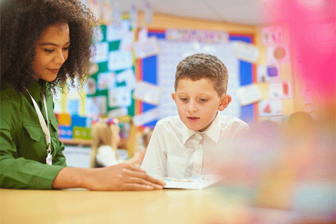 A primary aged schoolboy sits with his teacher in a one-on-one reading session. 